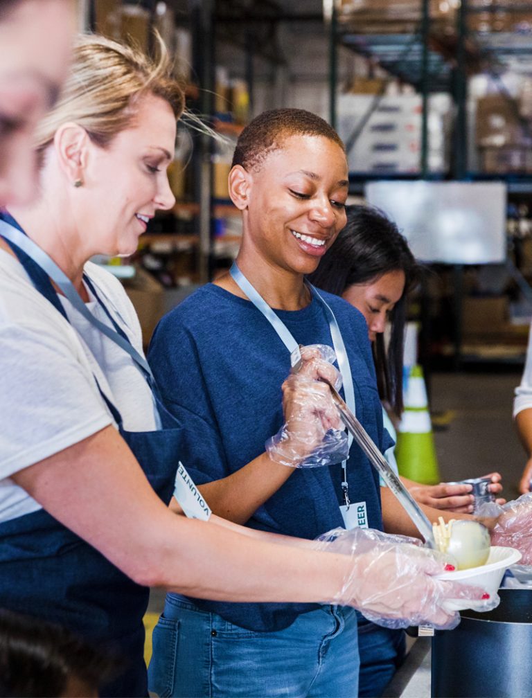 A white woman and a Black woman, both middle-aged, serving food at a soup kitchen